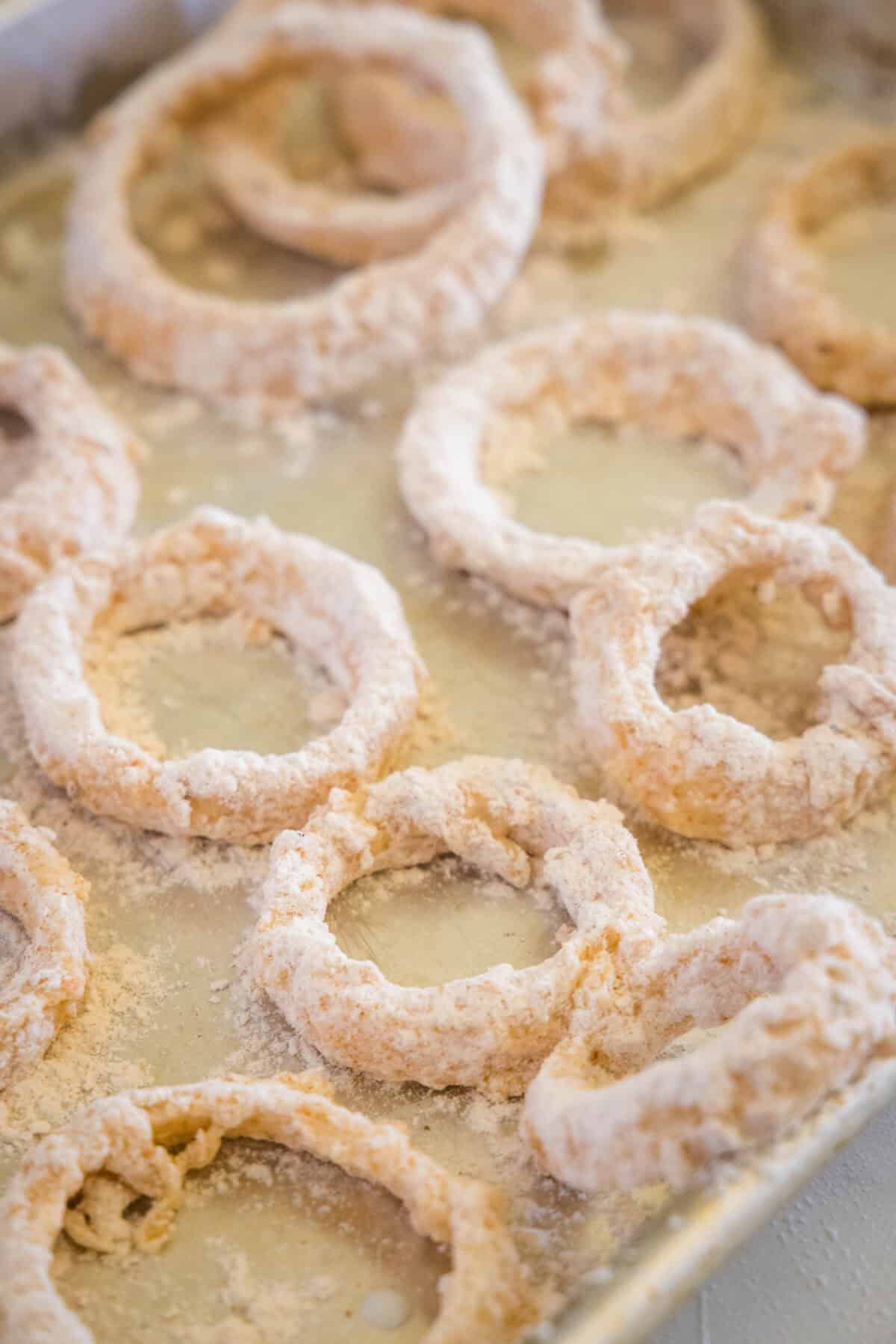 breading onion rings on a baking sheet ready for oil