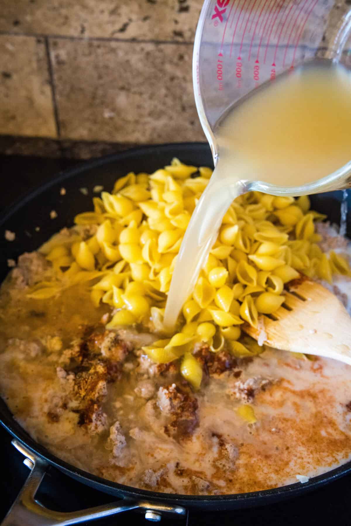 pouring in chicken broth to a skillet