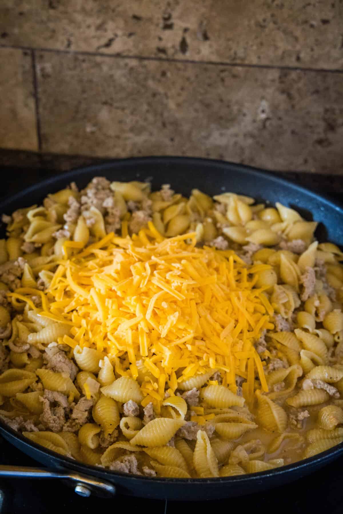 adding cheese to pasta in a skillet