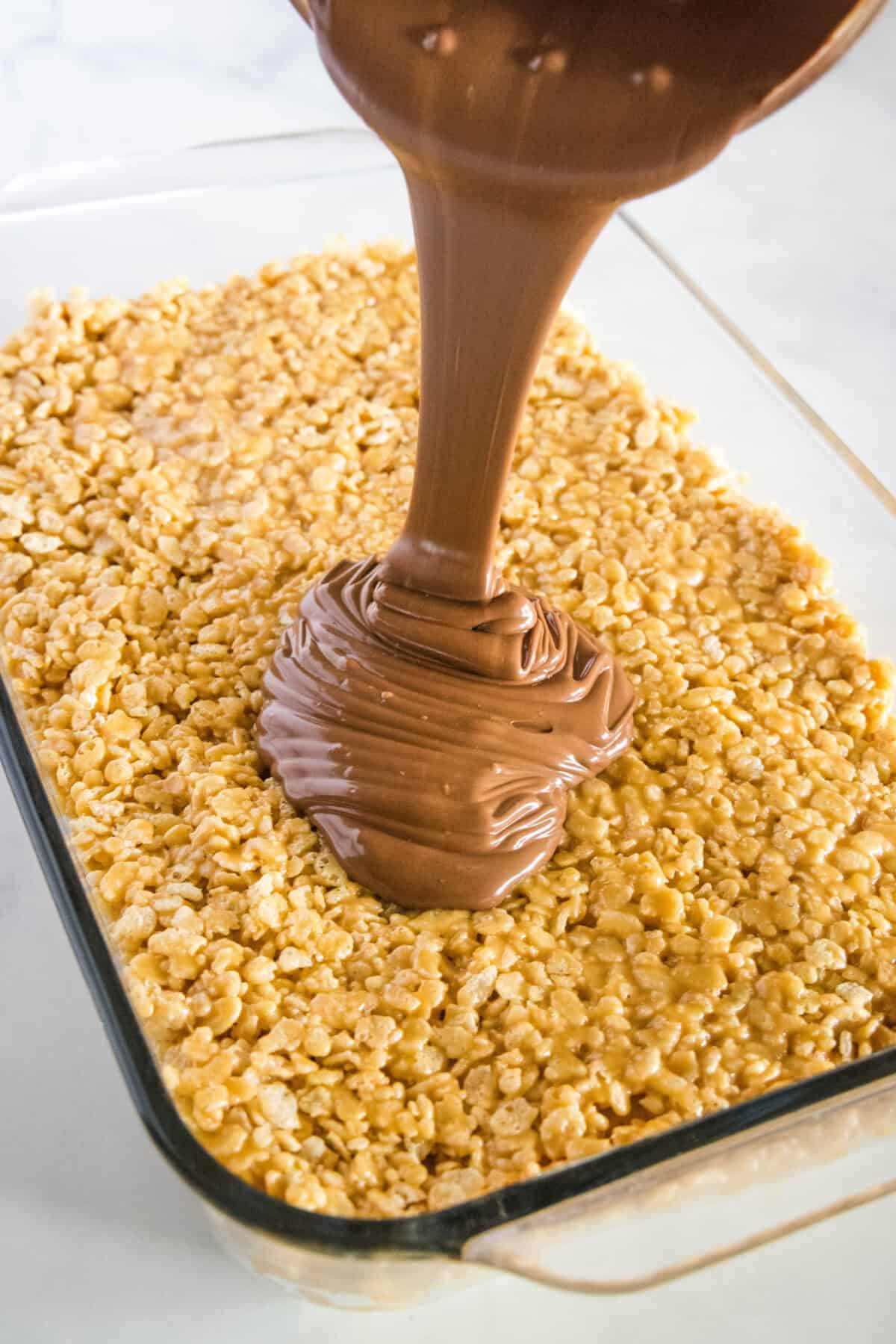pouring melted chocolate over rice krispie layer