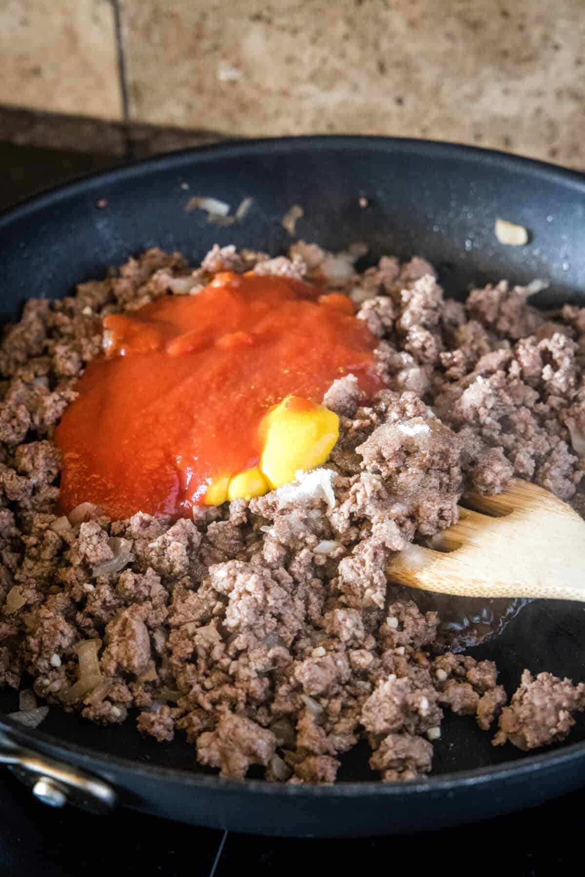 gound beef with tomato sauce and seasonings being added