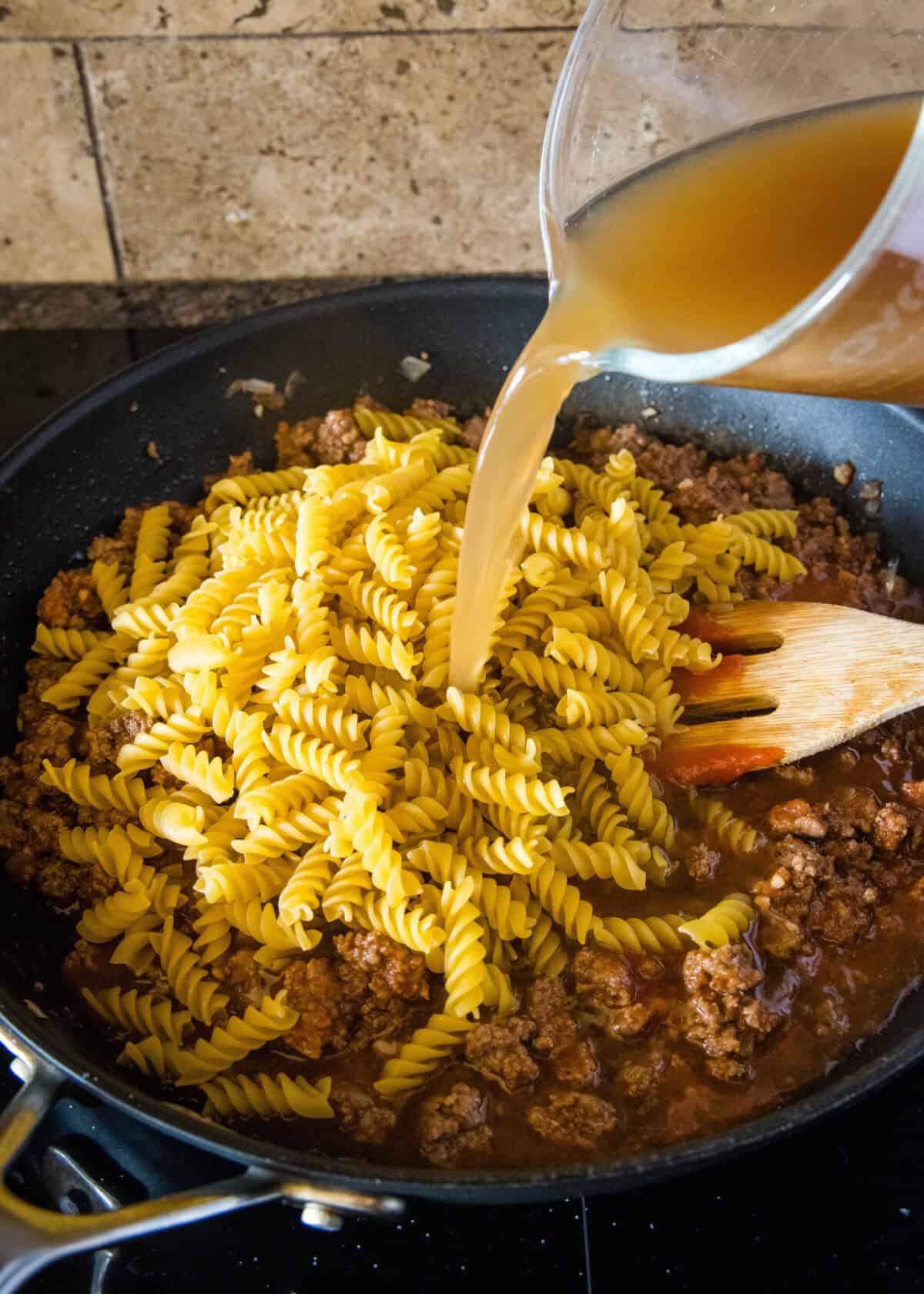adding dried pasta and broth to a skillet