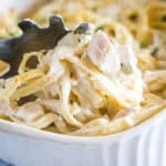 close up scooping baked fettuccine alfredo out of pan