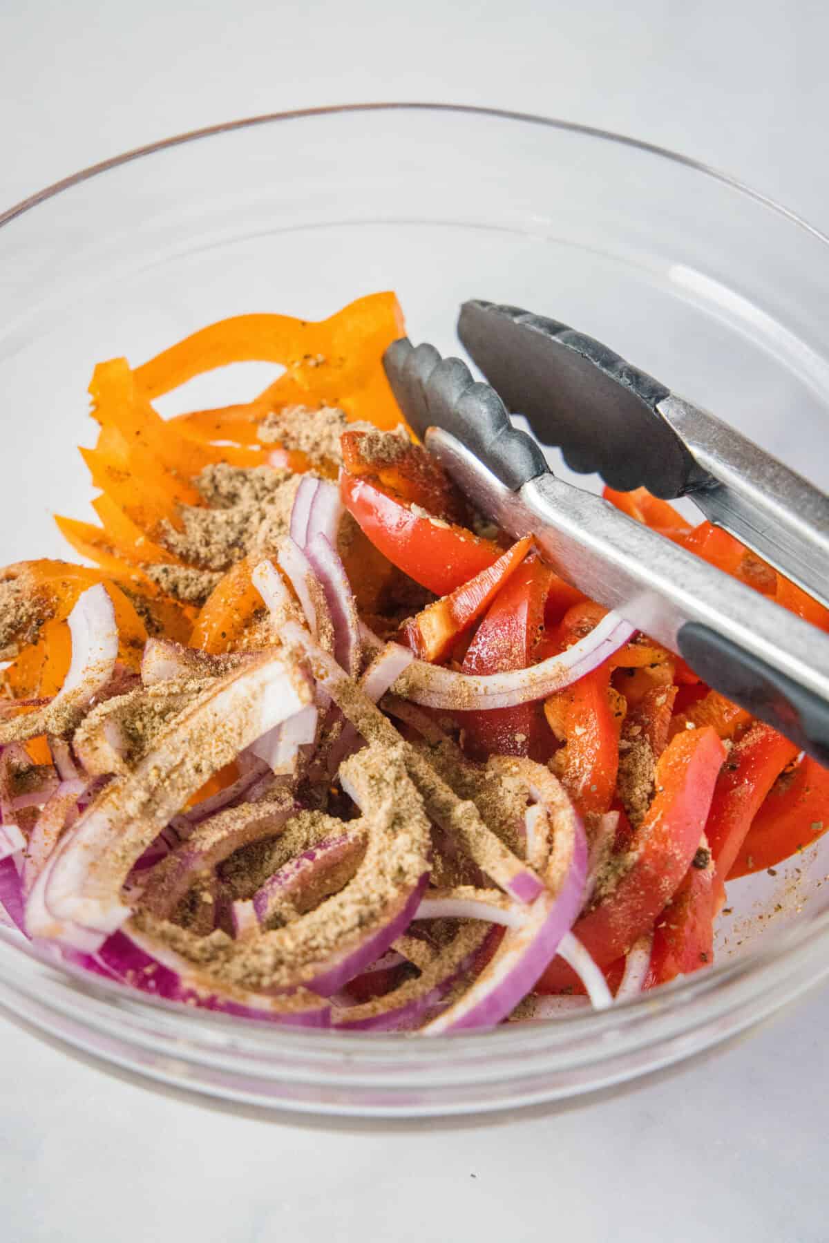 onions and peppers in a bowl with fajita seasoning