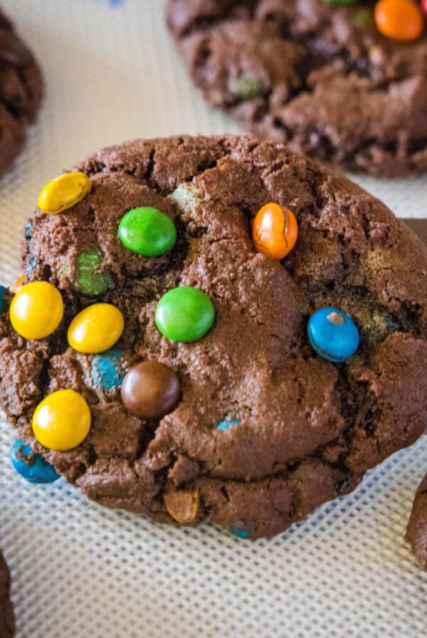 close up chocolate M&m cookie on a spatula above a baking tray