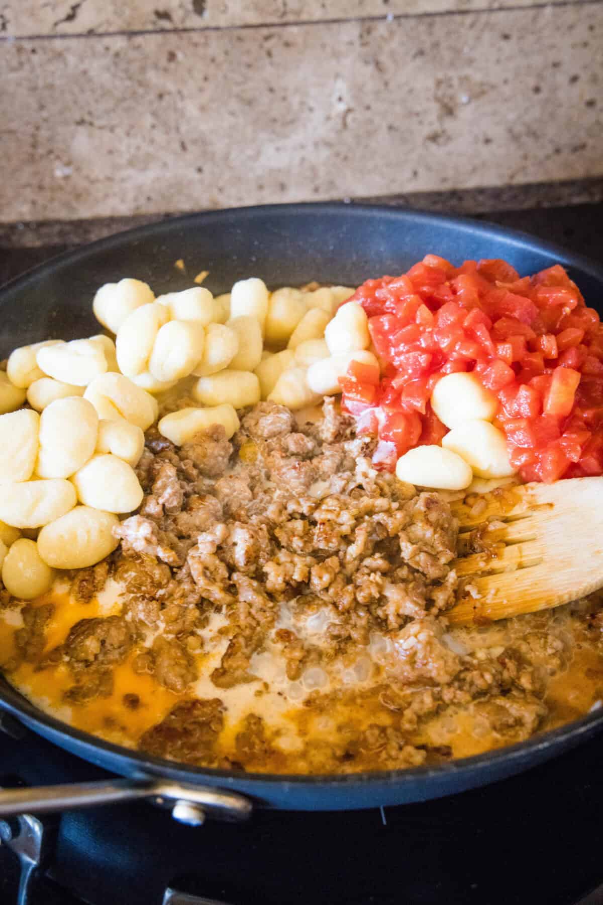 adding tomatoes and gnocchi to skillet with sauasage