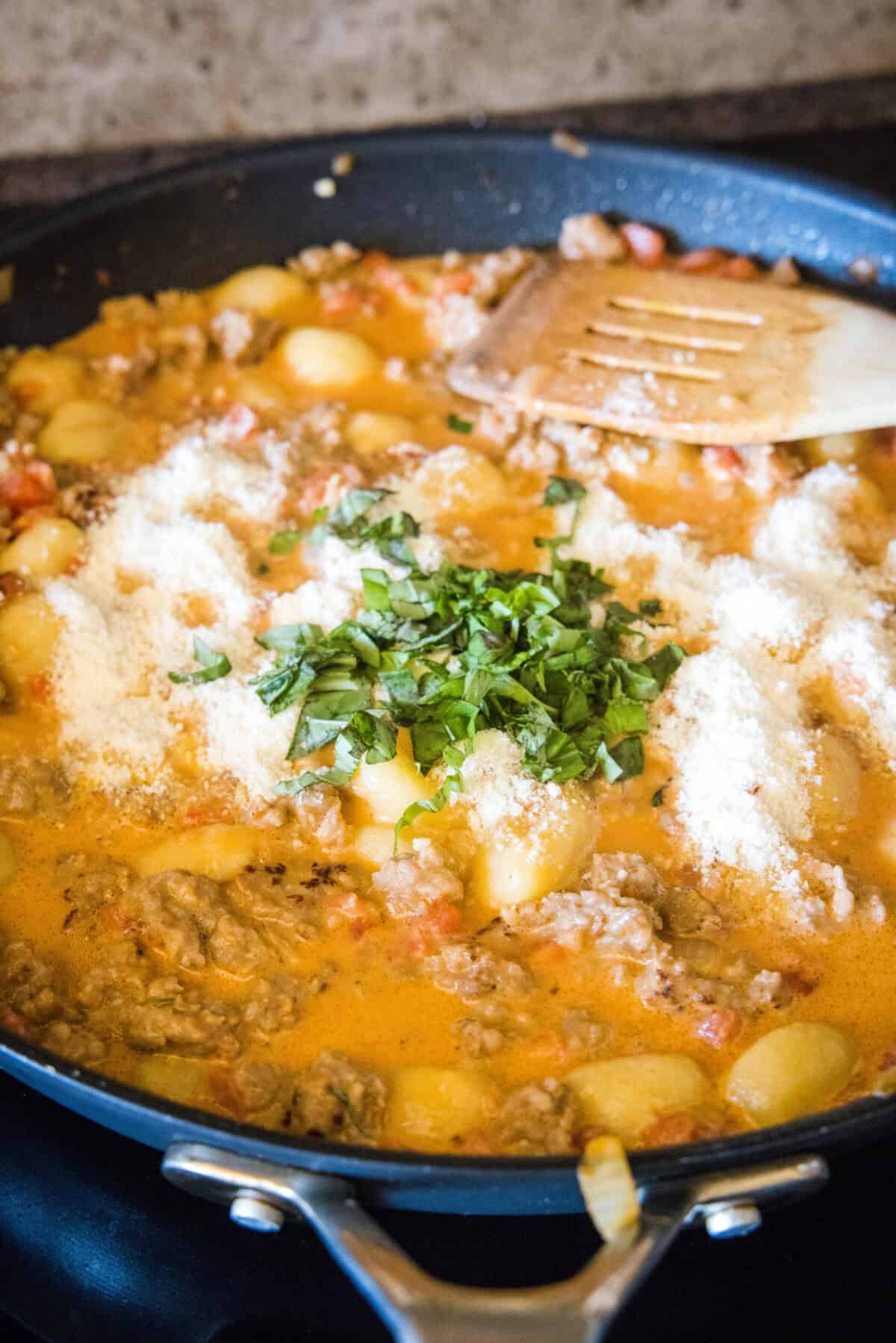adding parmesan cheese and basil to skillet with gnocchi