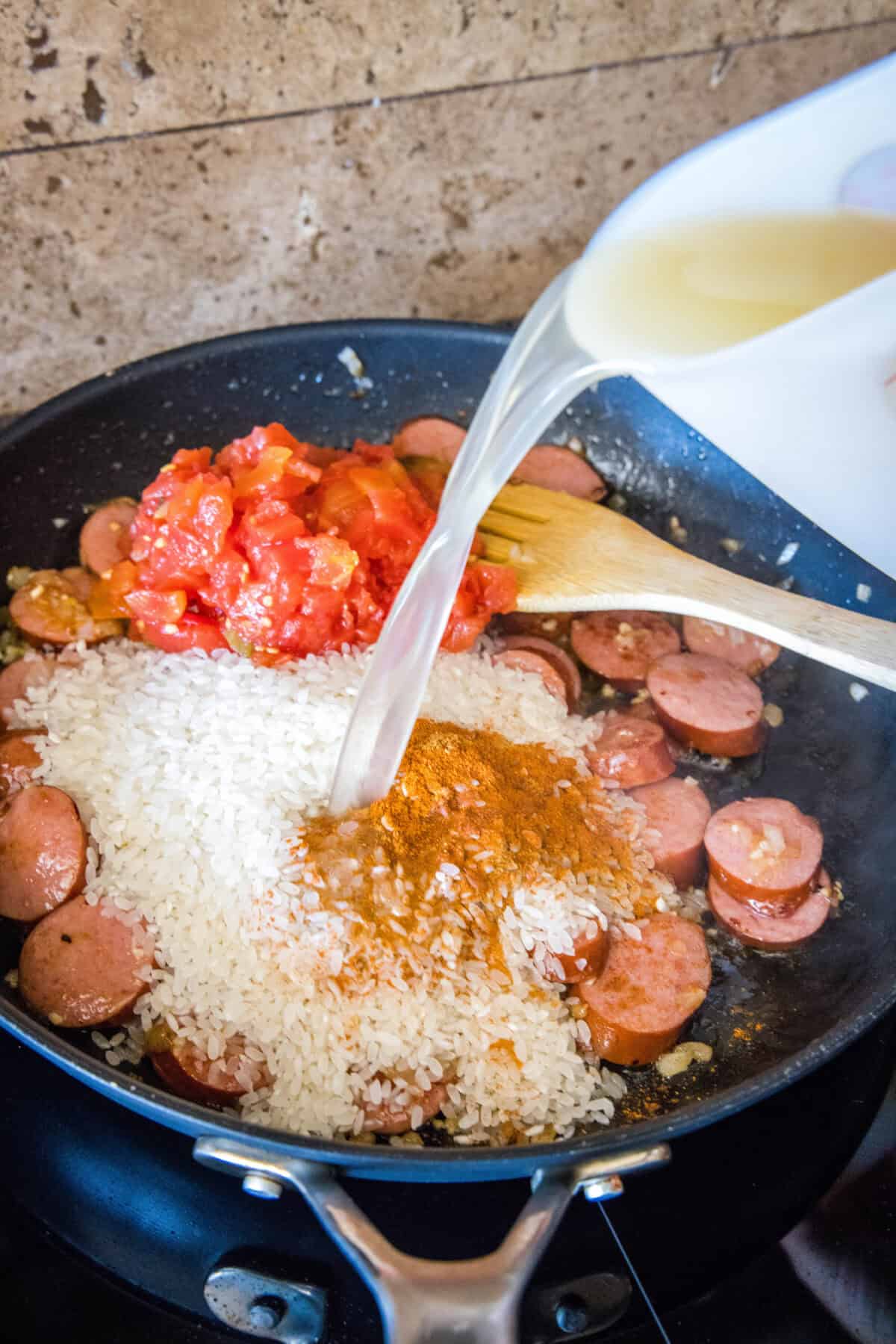 adding chicken broth, rice and tomatoes to skillet for sausage and rice