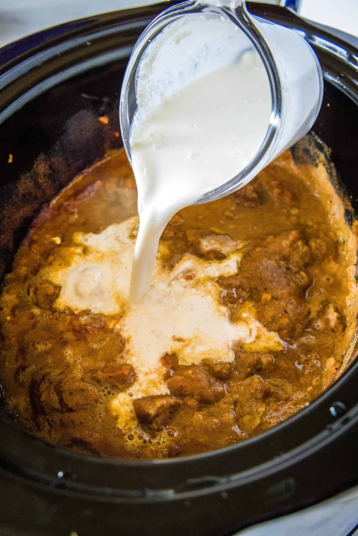 pouring heavy cream into tikka masala in crockpot