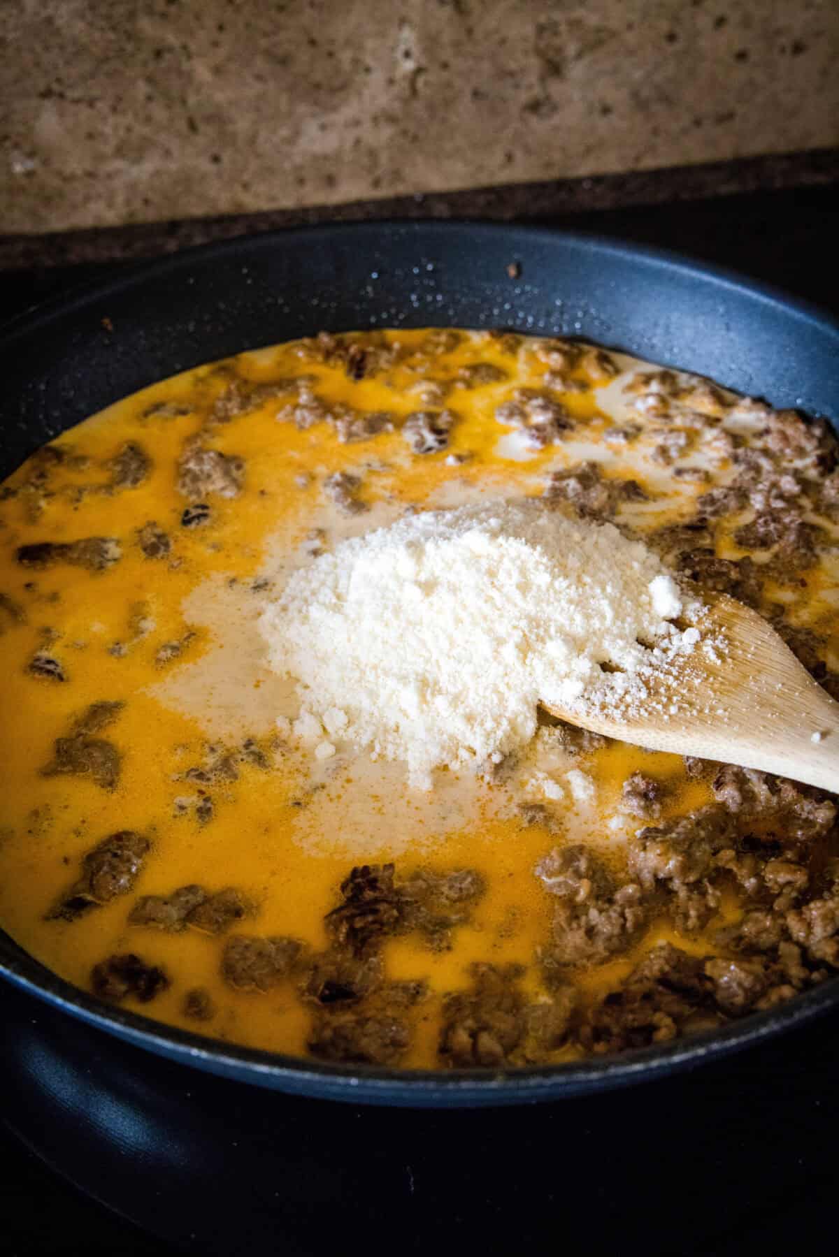 adding cream and parmesan cheese to skillet with sausage