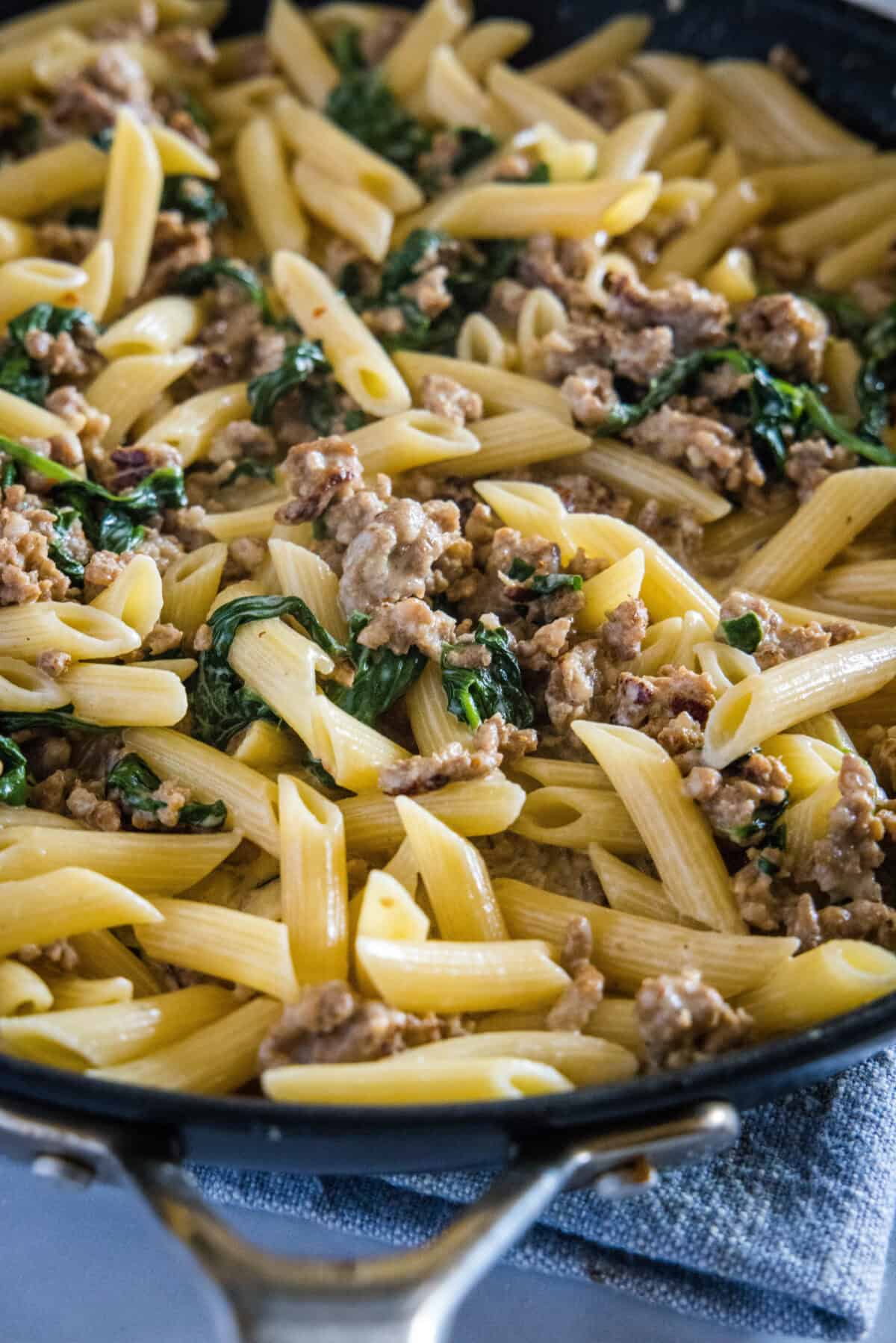 a skillet with sausage pasta with spinach