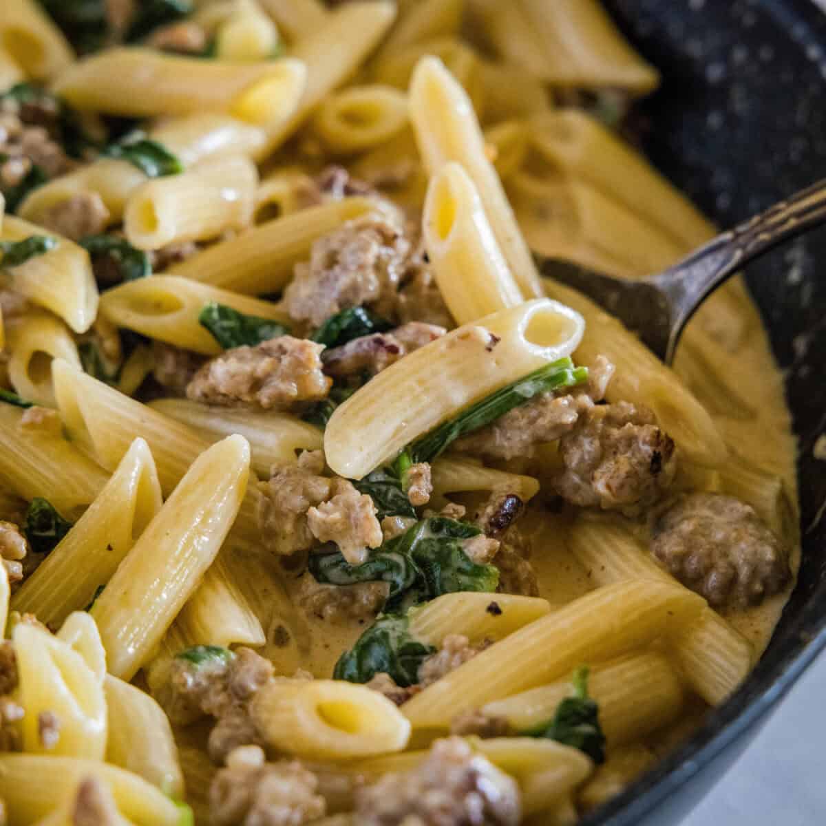 scooping sausage spinach pasta from the pan