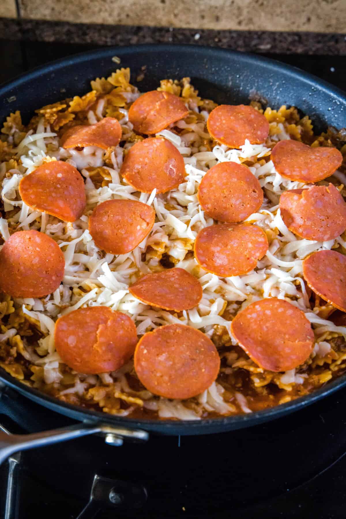 adding cheese and pepperoni to skillet over pasta