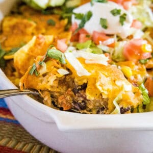 close up scooping chicken taco casserole from baking dish