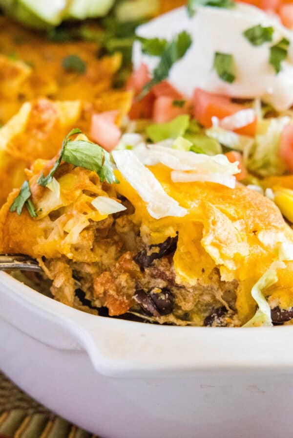 close up scooping chicken taco casserole from baking dish