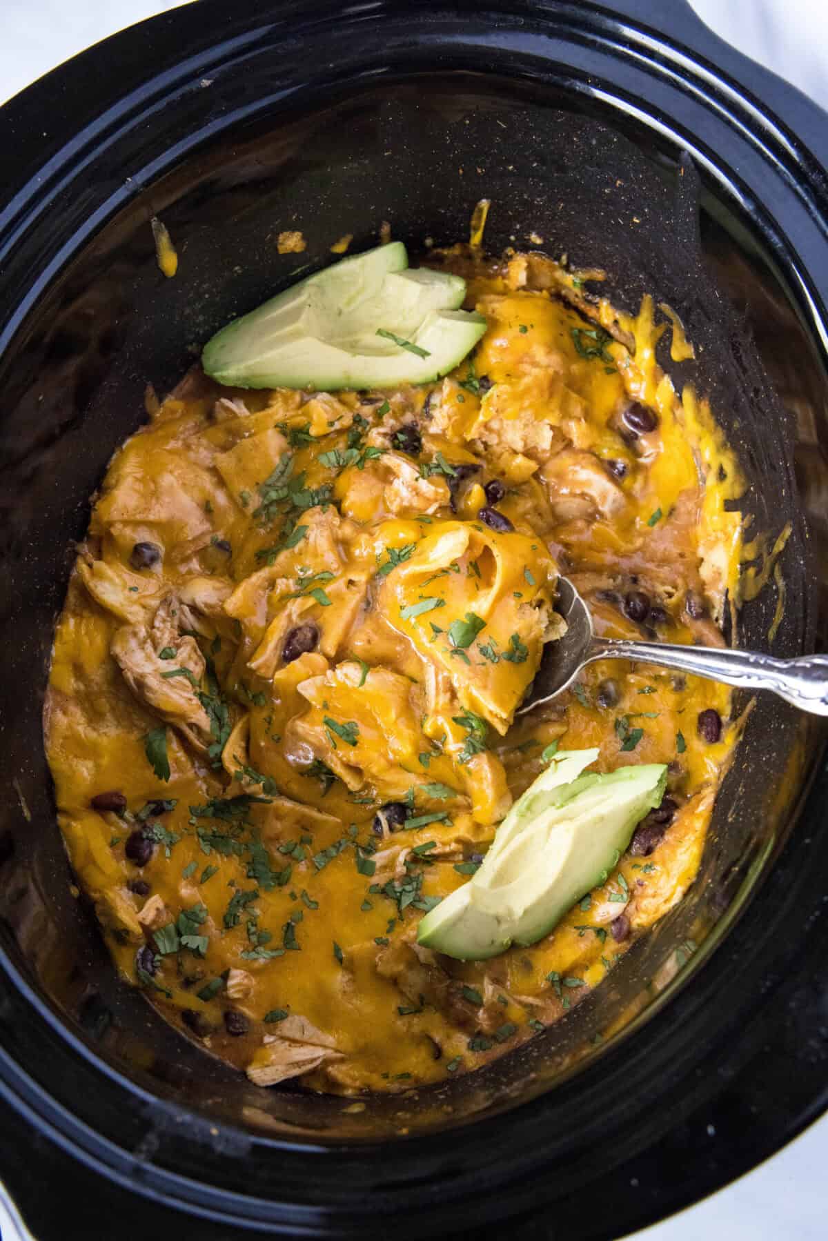 looking down at crockpt chicken enchilada casserole in slow cooker with a serving spoon