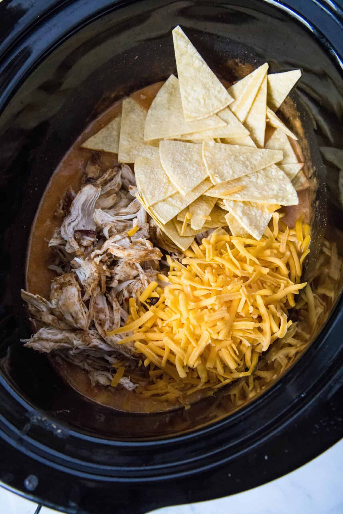 adding shredded chicken, tortillas and cheese to the crockpot