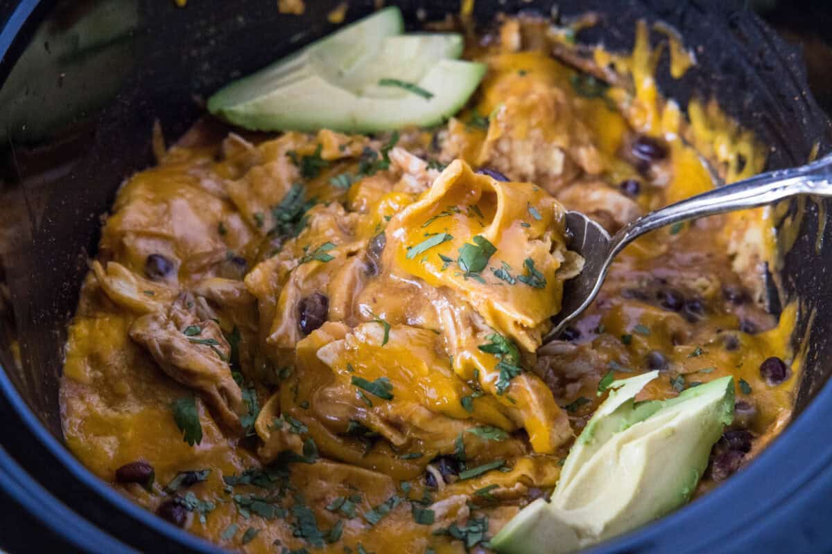 scooping crockpot chicken enchilada casserole out of the slow cooker