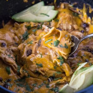 close up scooping chicken enchilada casserole from crockpot