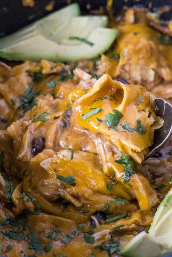 close up scooping chicken enchilada casserole from crockpot