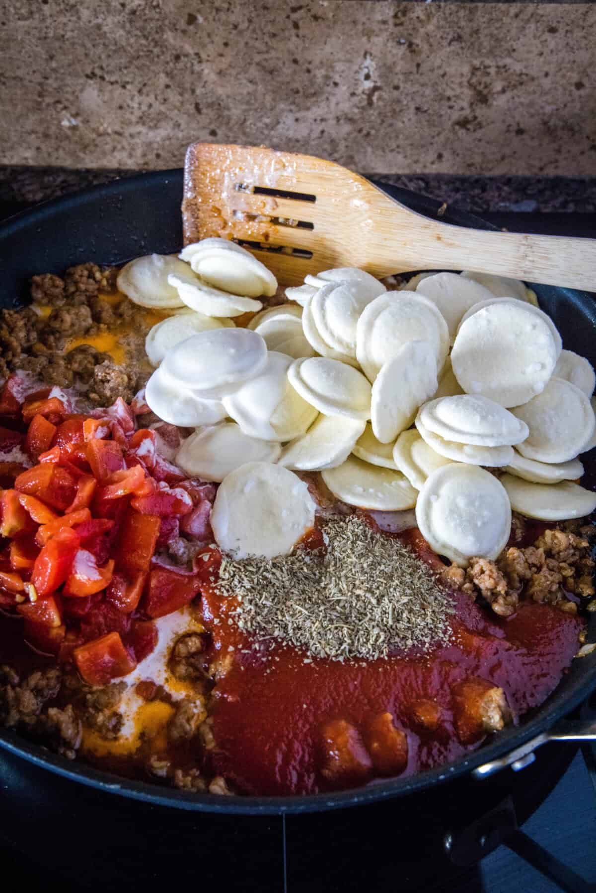 adding tomatoes, seasoning and ravioli to skillet