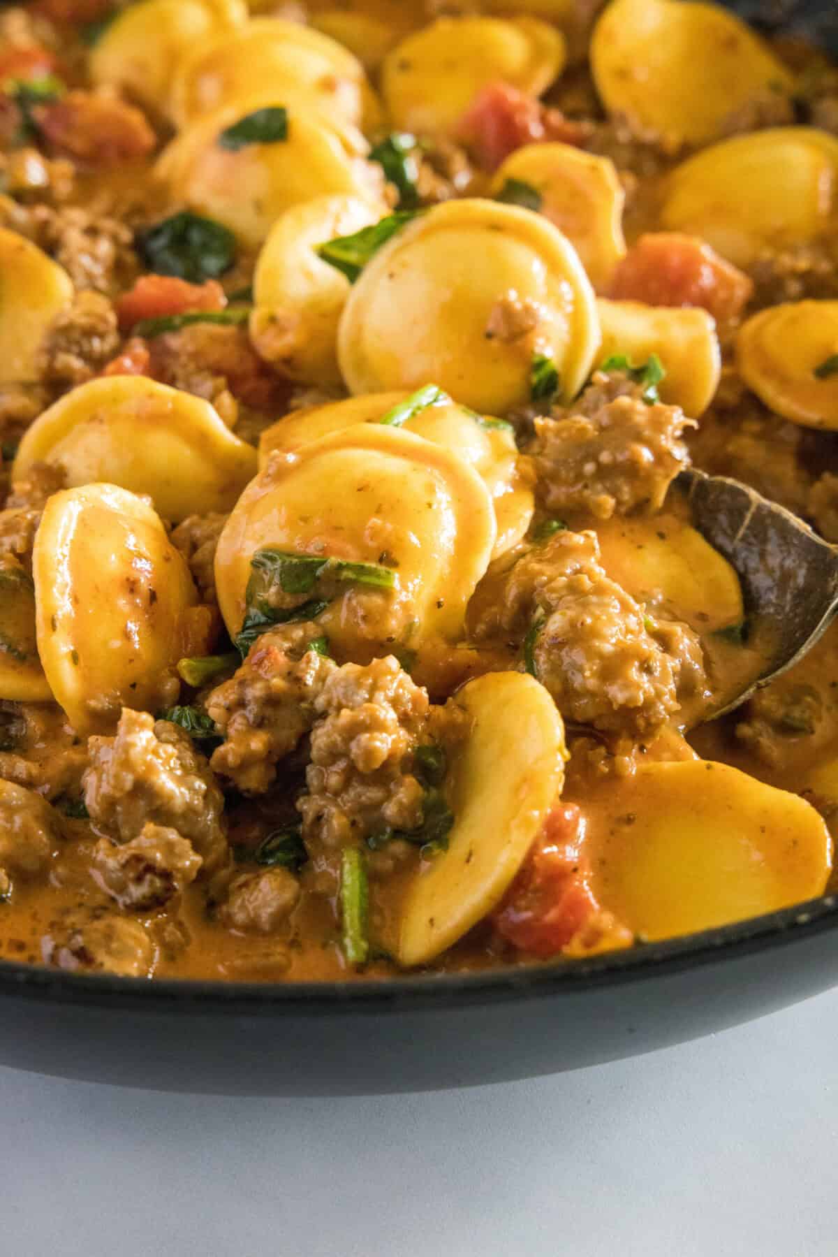 scooping ravioli with sausage from the pan
