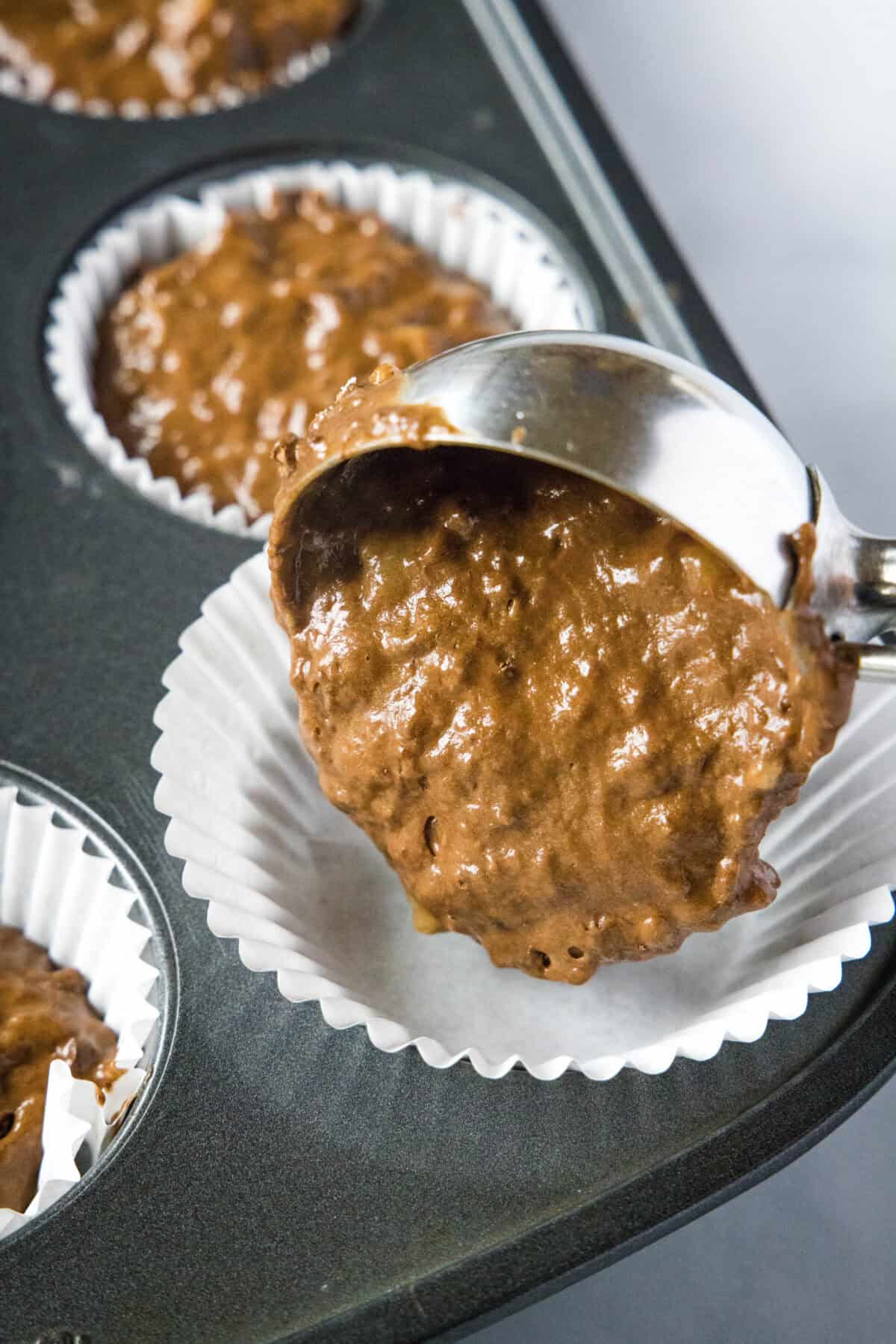 scooping chocolate banana muffin batter into muffin liners