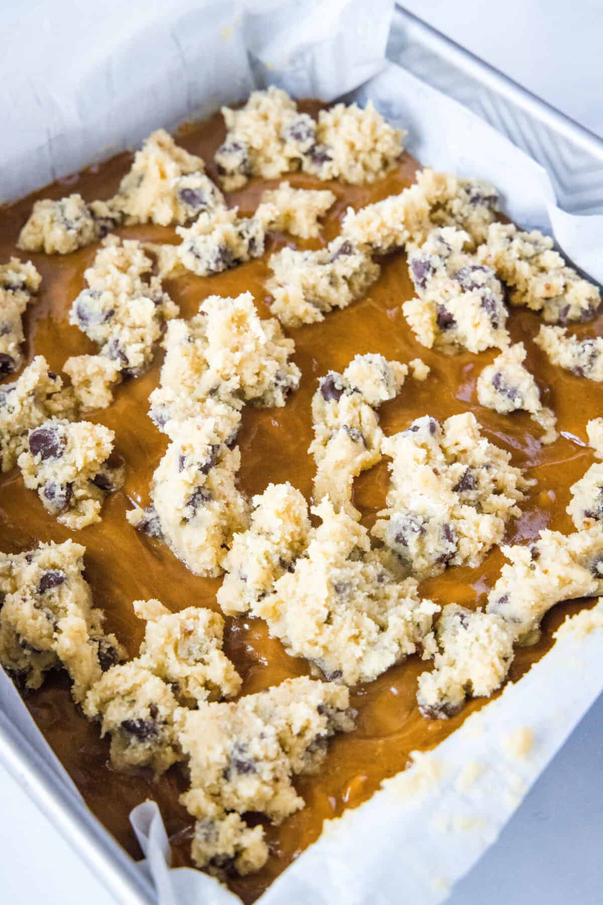 adding cookie dough over the caramel over bars in a pan