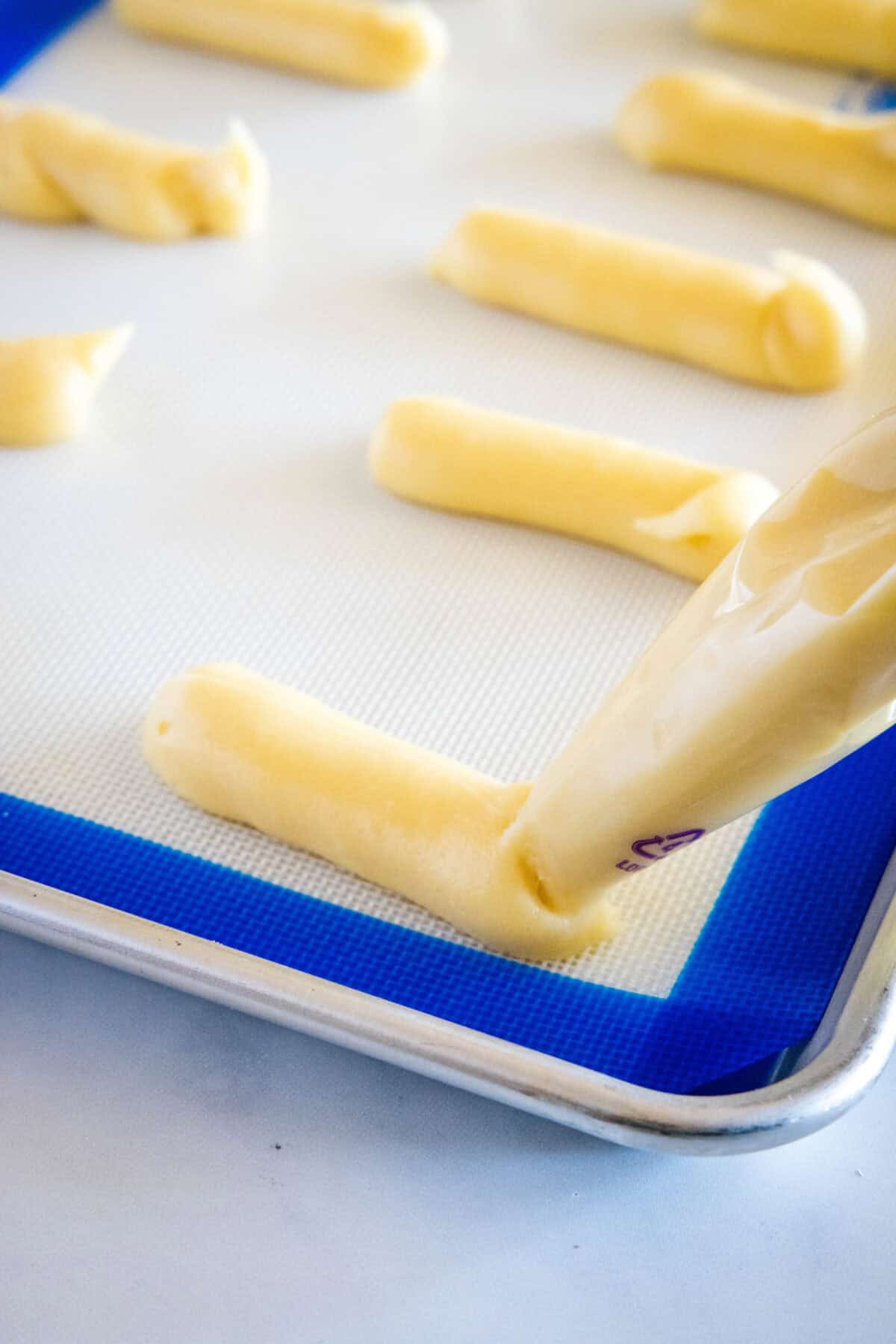 piping eclair dough onto baking sheet