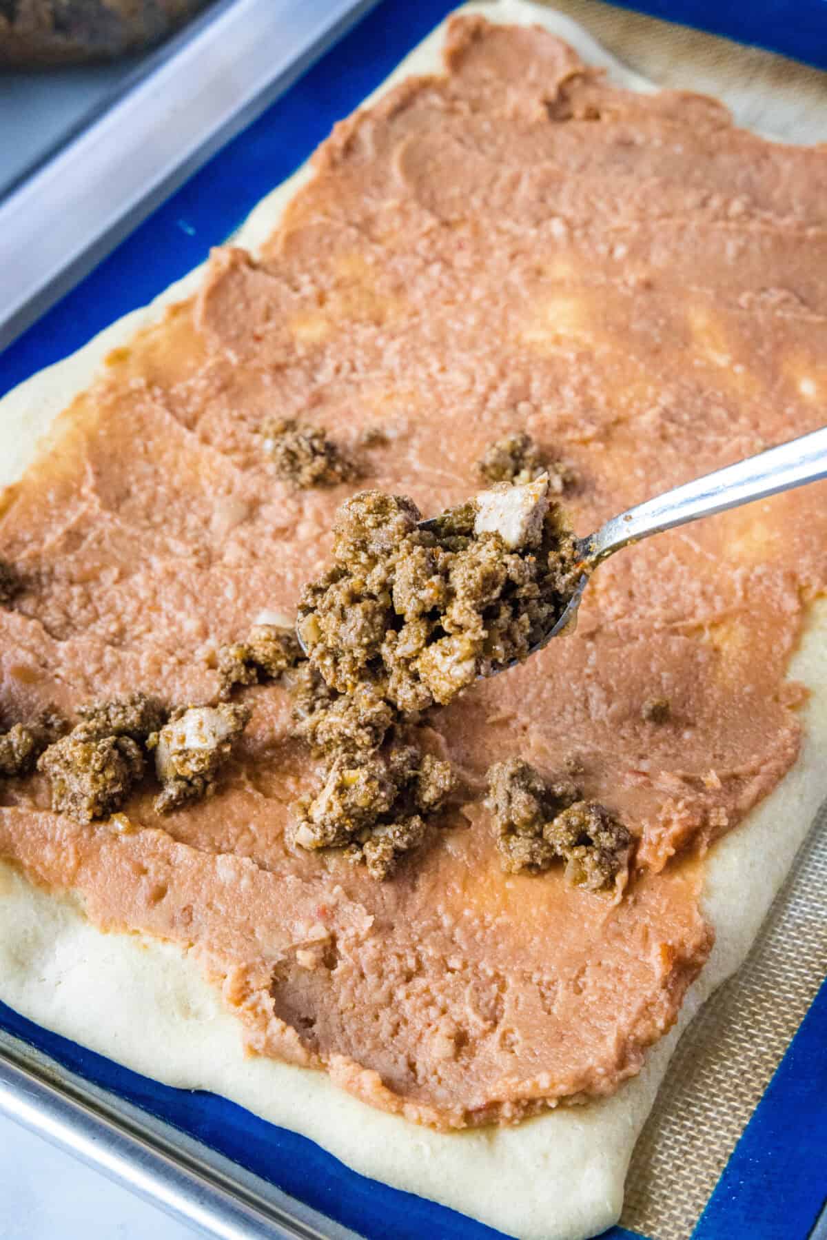 adding taco meat over beans on pizza crust