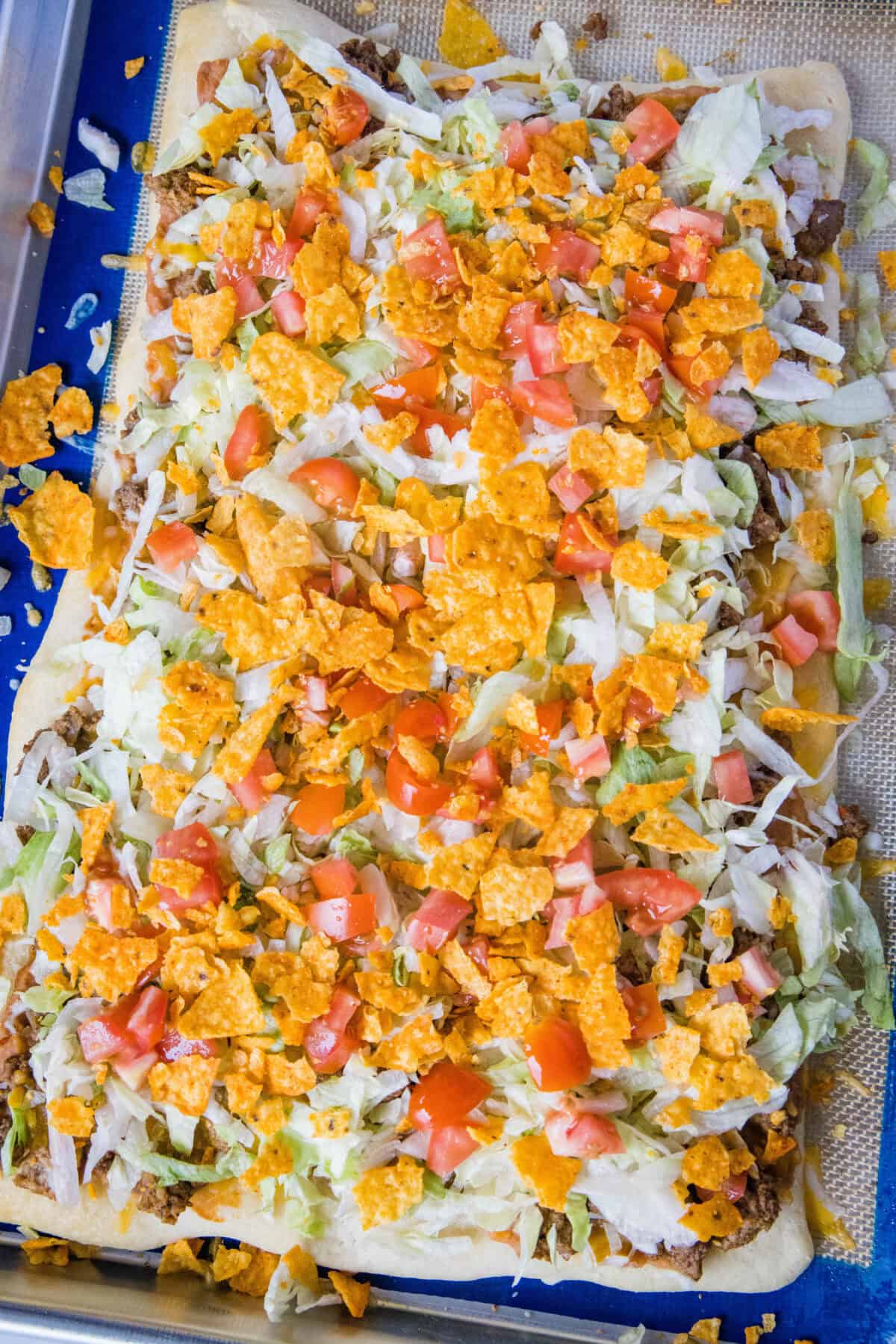 looking down on taco pizza topped with lettuce and tomatoes on a baking sheet