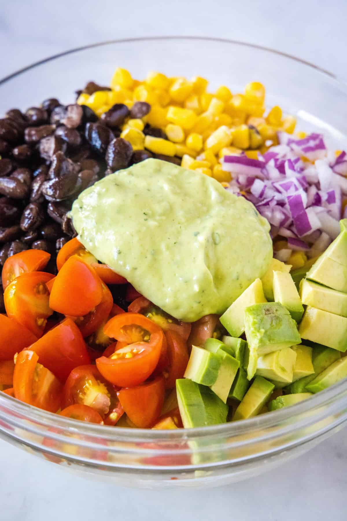 adding creamy avocado dressing to pasta salad