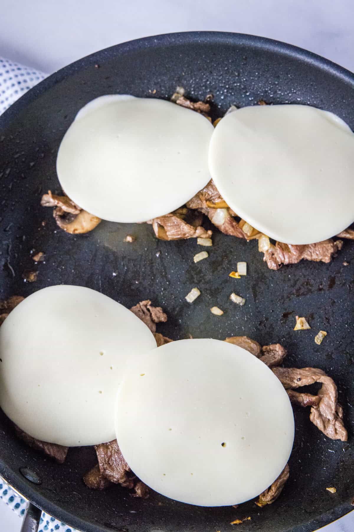adding cheese to steak mixture in pan
