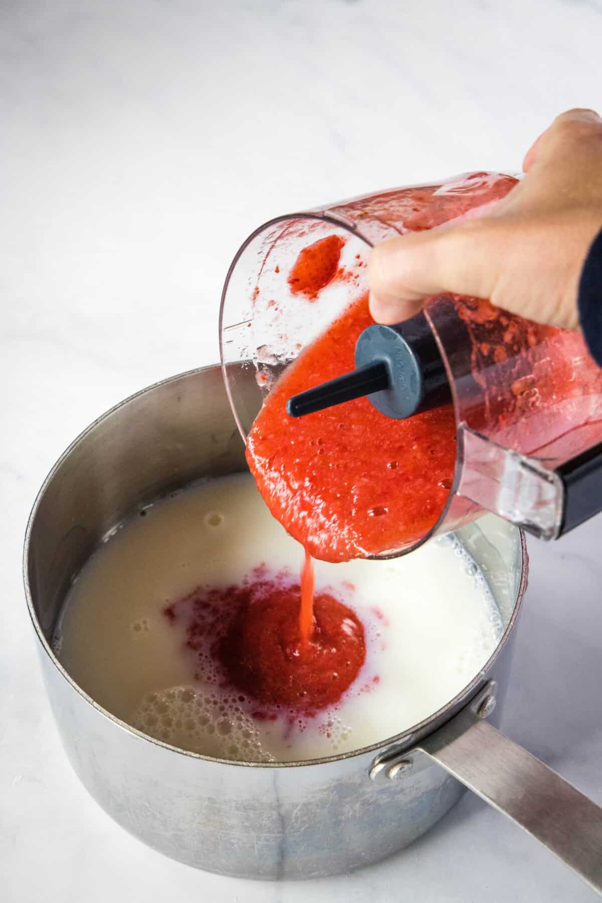 pouring strawberry puree into pan of milk