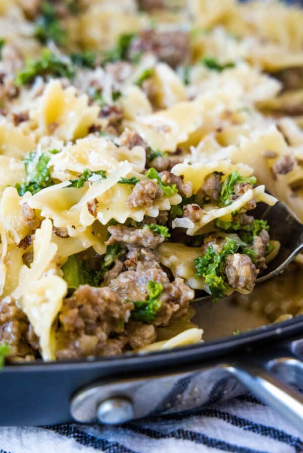 cropped close up scooping sausage kale pasta from the pan