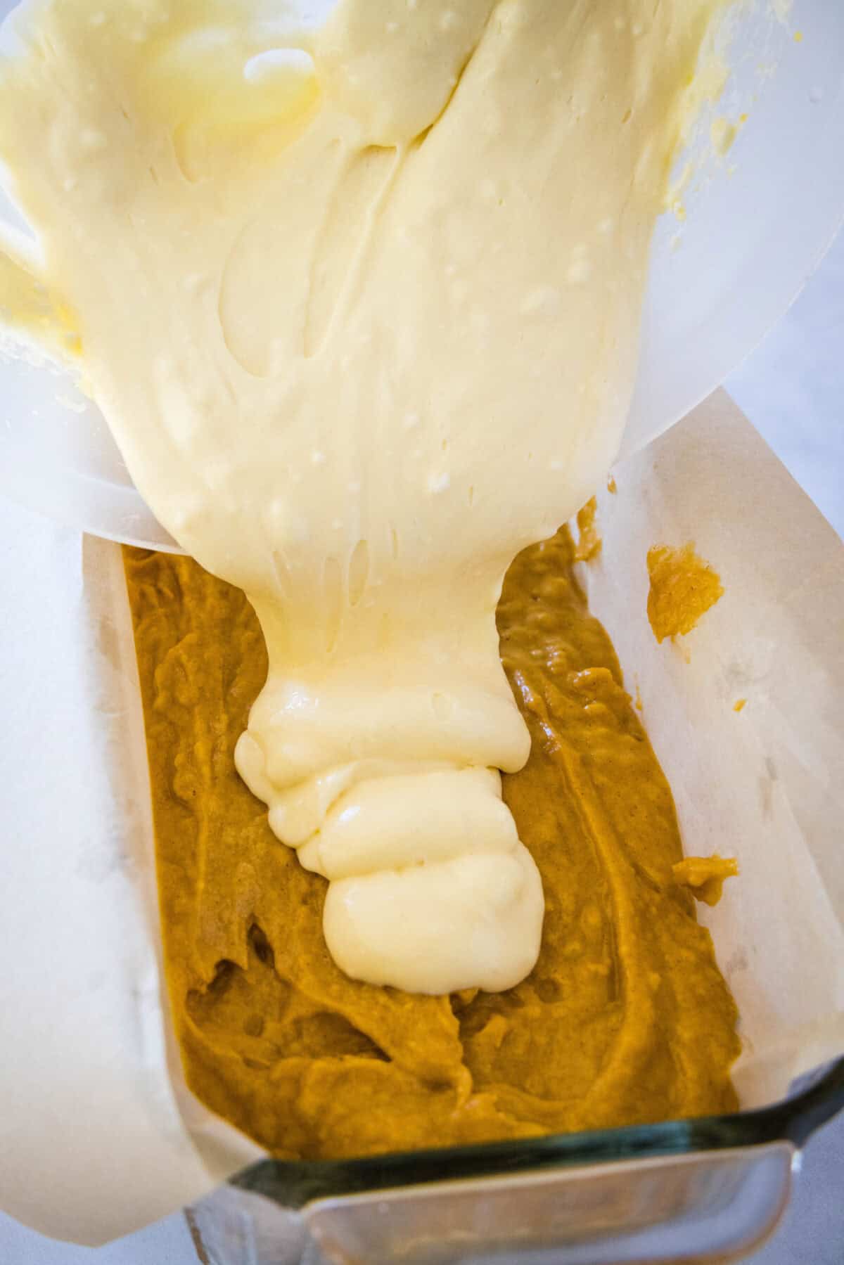 pouring cream cheese layer into pumpkin bread batter